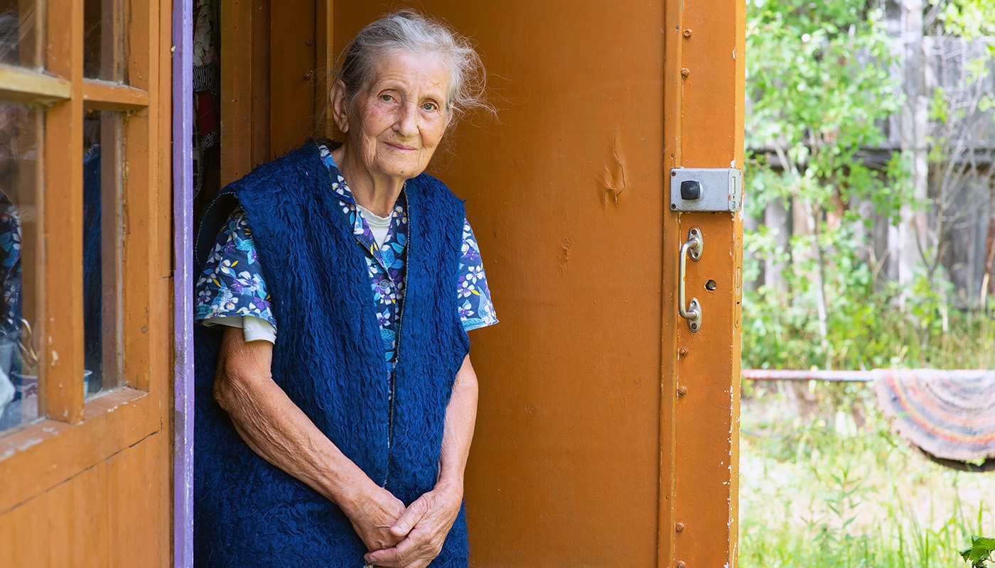 An older homeowner standing in the doorway of her restored home